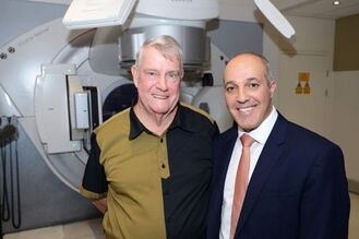 Two men standing together in front of a linear accelerator for cancer treatment.