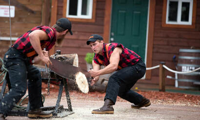 Picture of two lumberjacks wearing red and black flannel, team sawing a log