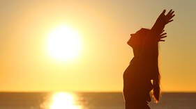 woman standing in sunset with hands above her head