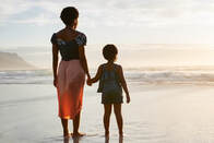 Mother and daughter holding hands looking at ocean