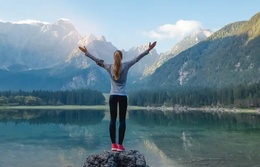 Woman Standing on Rock in power pose facing a lake and mountains